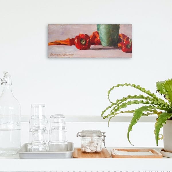 Oil painting of red peppers, a green copper vase juxtaposed with an orange fabric all arranged on a grey background displayed on a wall.
