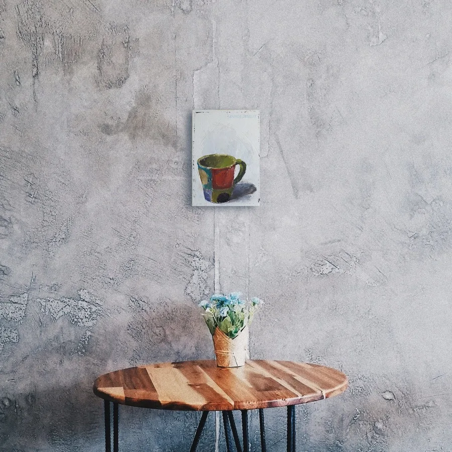 Oil painting of a colorful mug set on a light grey background displayed on a wall.
