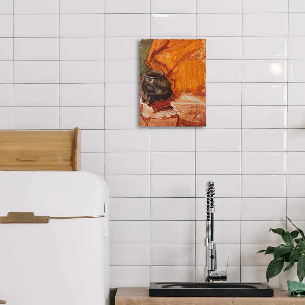 Oil painting of a black cauldron set in a background of orange and green fabric displayed on a kitchen wall.
