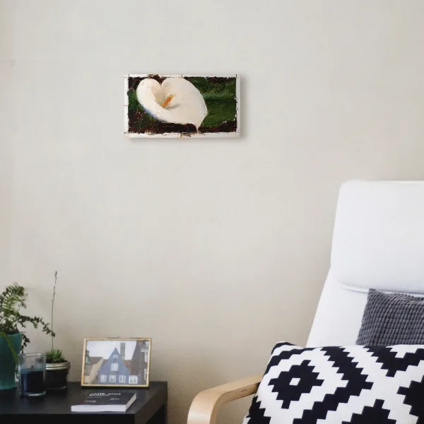 Oil painting of a white calla lily with yellow pistol tightly framed in warm dark brown background displayed on a wall.