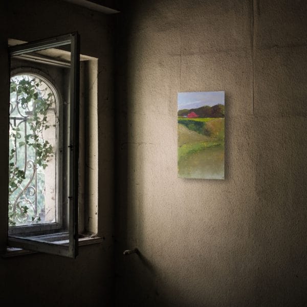 An oil painting of a red barn set in a green hilly landscape displayed on a wall.