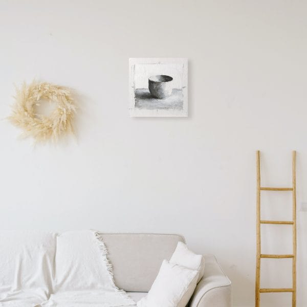 Monochromatic oil painting of a white cup on a white background with black and grey shadows displayed on a wall.
