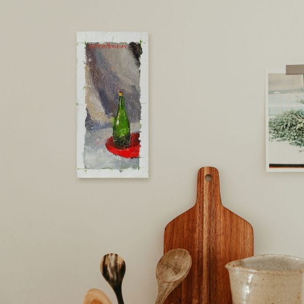 Oil painting of a green bottle arranged on a bright red table fabric with a grey backdrop as shown on a wall.