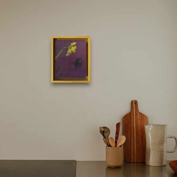 An oil painting of a bright yellow daffodil casting a shadow on a dark purple background as displayed on an interior wall.