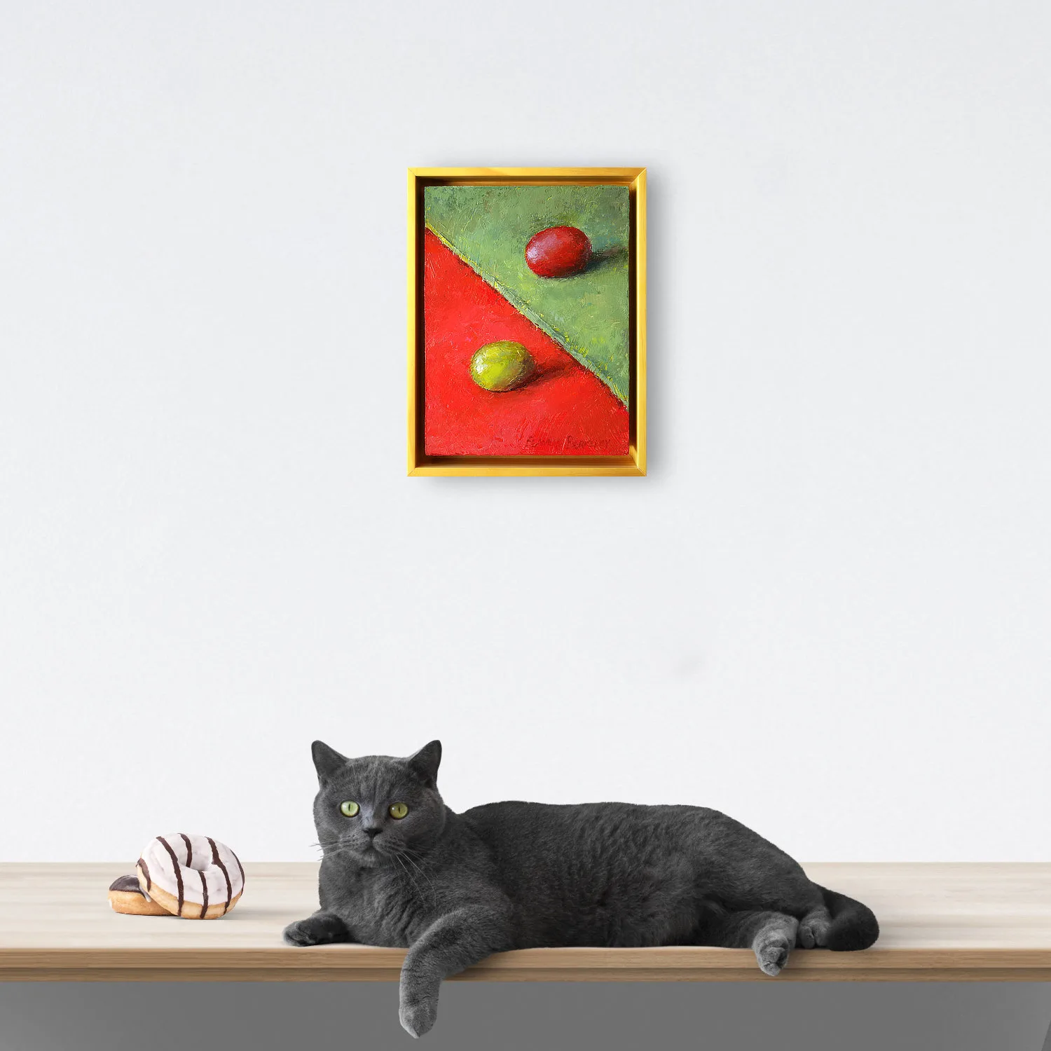An oil painting of a green grape on red fabric juxtaposed with a red grape on a green fabric as displayed on an interior wall.