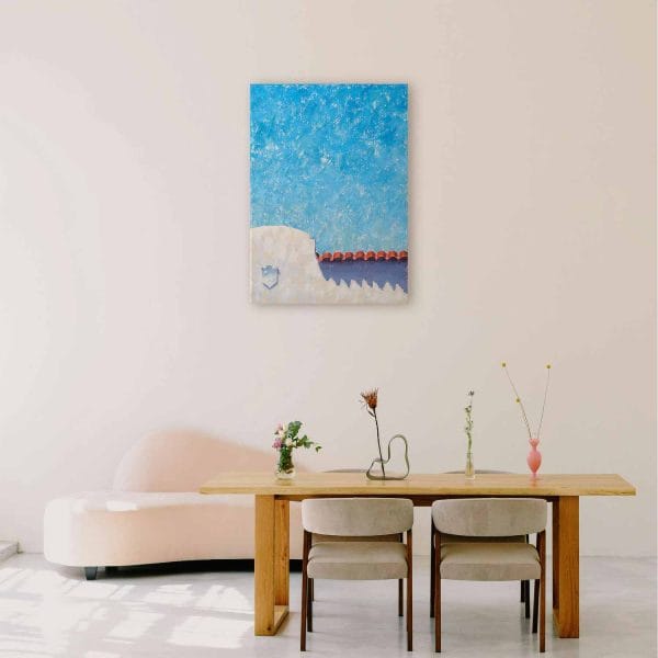 An oil painting of a Spanish colonial style white building with red tile roof juxtaposed below a bright blue sky as displayed on an interior wall.