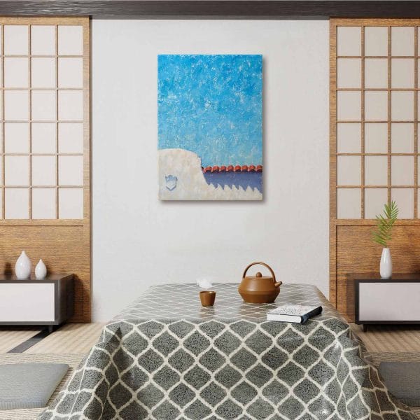 An oil painting of a Spanish colonial style white building with red tile roof juxtaposed below a bright blue sky as displayed on an interior wall.