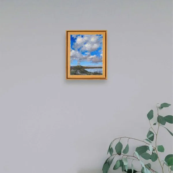 An oil painting of white puffy clouds in a deep blue sky rising above the Cerro Pedernal, near Ghost Ranch, Abiquiu, almost seem as if the clouds emerge from this ancient volcanic formation in this landscape of water, mountains, clouds, and sky as displayed on an interior wall.