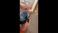 Two hands using a yellow and black drill to set a screw into a wooden frame for a painting.