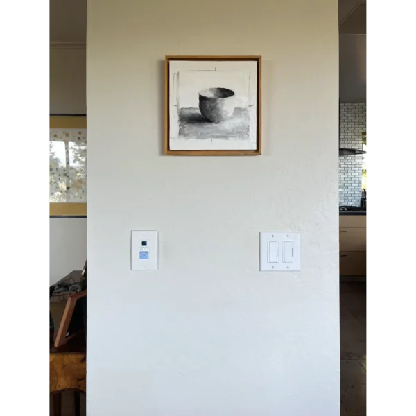 An oil painting of white cup on a white surface and white background using monochrome greys as displayed on an interior wall.